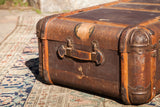 Patinaed rusty orange bent wood and decorative metal corner of the vintage Indestructo trunk.
