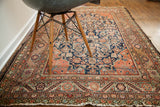 Angled perspective of worn antique Feraghan rug, showing rich indigo and coral Herati pattern.