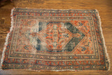 Distressed fringed corner of an antique Persian tribal rug, showing geometric borders and terracotta navy hues.