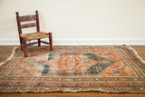 Antique Persian tribal medallion rug with worn orange, blue, and cream patterns, 3x4.7 feet.