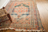 Antique worn tribal rug's decorative fringed corner, showing textured pile in coral, blue, and beige.