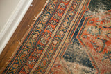 Antique tribal rug close-up: worn geometric border in deep orange and navy hues.