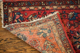 Vintage small red rug corner displaying color wear and its finely woven patterned foundation.