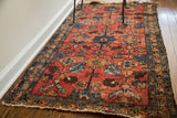 Angled view of the red Lilihan Sarouk rug, with floral motifs and visible tattered fringe.
