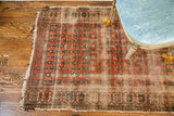 Antique rug's repeating rust and navy floral pattern shows storied, worn aesthetic.