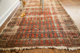 Close-up of antique rug's worn repeating red floral pattern, abrash, and tattered fringe.