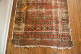 Antique worn rug corner detail: tattered fringe, faded coral and blue repeating floral design.
