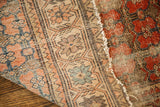 Detail of antique rug showing worn repeating floral design, abrash, and tattered red sections.