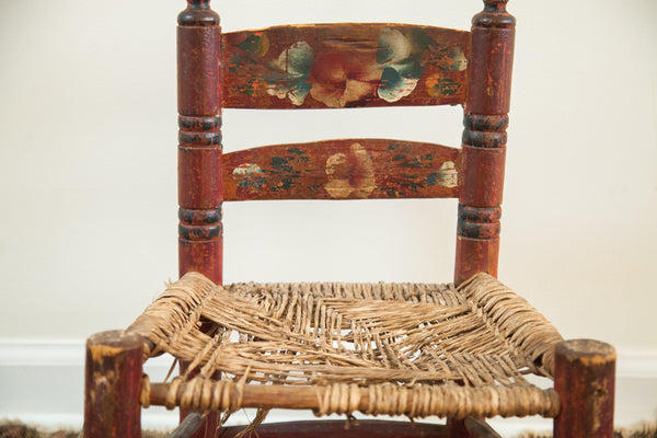 Close-up of the hand-painted backrest and worn woven rush seat of a folk art chair.
