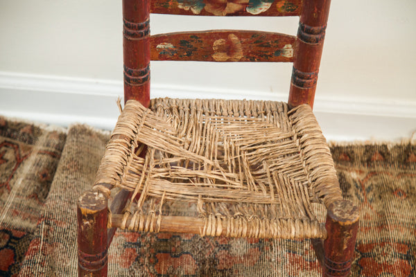 Detailed view of the worn rush seat on the antique, hand-painted child's chair.