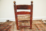 Distressed red paint and worn rush seat on the back of a primitive child's chair.