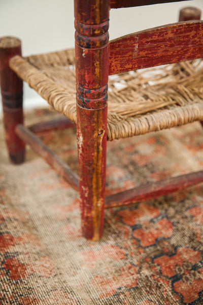 Close-up of the hand-carved leg with chippy red paint and worn rush seat corner.