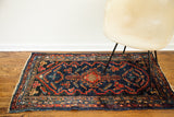 Vintage Lilihan rug corner, deep indigo blue and terracotta red geometric pattern with fringe.