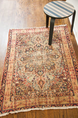 Distressed corner of antique Lavar Kerman rug, revealing faded floral motifs, cypress trees, and fringe.