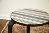 Alvar Aalto style side table with intricate striped top and visibly chipped black edge.