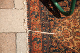 Exposed foundation on an antique Persian Senneh rug with rich terracotta and navy herati pattern.