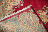 Vintage Kerman rug corner reveals ruby red pile and cream border with soft florals.