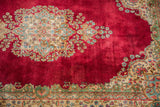 Intricate floral motifs in beige, blue, green on the cochineal red field of a Kerman rug.