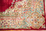 Vibrant ruby red field meeting a traditional Kerman border with teal, pink, and beige florals.