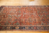 Antique Fereghan carpet close-up, rust field with allover flowering vine design and deep blue border.