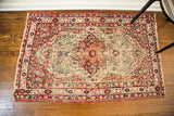 Worn antique Kerman rug corner, featuring distressed red geometric border and cream fringe.