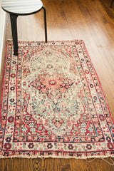Distressed antique Kerman rug corner, with angular red, cream, and blue border motifs and fringed edge.