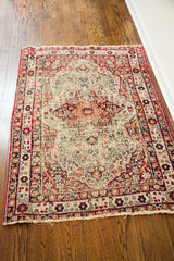Antique Kerman rug corner displaying angular red border and distressed patterned field.