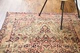 Antique Kerman rug corner, showcasing blanched coral and navy curvilinear floral patterns on beige.