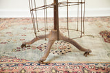 Rusty metal base and claw feet of the dress form, standing on a vintage floral rug.