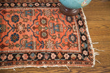 Aged fringe and dark floral border on the corner of the worn red Persian Lilihan rug.