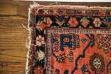 Worn red Lilihan rug corner, showing colorful geometric borders and frayed fringe.