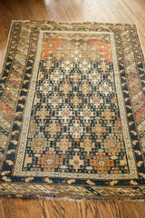 Geometric dark blue, beige, and orange patterns on antique Caucasian rug corner, with fringe.