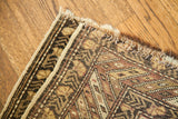 Aged corner and fringe of an antique Caucasian rug with geometric dark blue and muted orange patterns.
