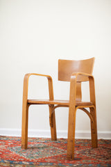Angled view of Thonet bent plywood chair, showing contoured armrest and back chip.