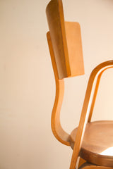 Detail of the Thonet bent plywood chair's curved backrest, light wood, and small chip.