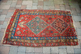 Antique Heriz fragment corner: vivid plum medallion, red field, blue border, and natural fringe.