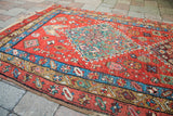Angled view of an antique Heriz rug fragment, featuring vibrant red, teal central design, and blue border.
