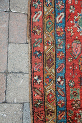 Woven edge and vivid red, blue, gold geometric motifs of the antique Heriz fragment rug.