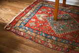 Vivid red geometric field and layered blue, green borders on an antique Persian Heriz fragment.