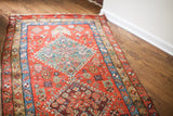 Antique Heriz rug fragment showing vivid red, teal blue, and plum geometric patterns.