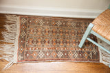 White fringe and geometric pattern in muted grey and orange on a vintage Afghani rug.