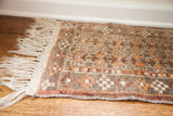 Rug corner with natural fringe, highlighting the geometric grey, brown, and orange pattern.