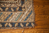 Geometric tribal patterns and earth-toned frayed edge on an antique Caucasian rug corner.