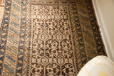 Antique Caucasian rug detail: geometric charcoal motifs, light earth-toned field, blue accents.