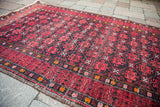 Geometric Afghani runner rug with a cranberry red field and dark charcoal pattern.