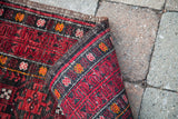 Geometric cranberry red and charcoal pattern on the rolled edge of the Afghani rug.