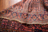 Folded vintage Persian Lilihan rug's worn fringe, raspberry field, and navy tree motifs.