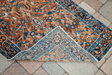 Antique Yezd rug corner folded back, revealing intricate blue and beige reverse patterns and fringe.