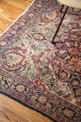 Antique Persian Kerman rug corner showcasing traditional curvilinear florals in red, blue, cream tones.