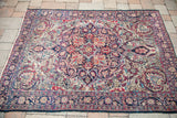 Antique Kerman rug's corner displays intricate red, blue floral motifs and a dark sapphire border.